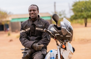Amos Lungu, a school feeding officer from Zambia, sits on a motorbike
