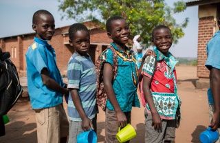 Four boys outside in Malawi standing with mugs