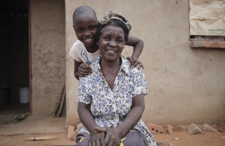 A grandmother, Elly, sits, while her granddaughter, Grace, stands behind her
