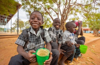 Boys in Zambia sit outside with mugs of Mary's Meals