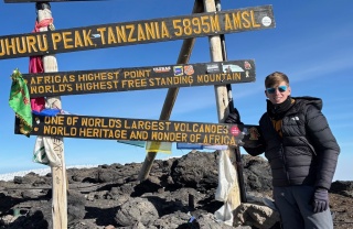 Teenager Lochlan stands at a sign signalling that he is at the summit of Mount Kililmanjaro