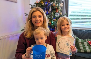 Victoria and her children in a living room, a boy holds a Mary's Meals mug and a girl holds a Santa plate
