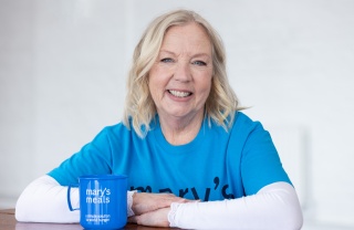 Deborah Meaden sitting smiling with her arms leaning on a table, next to a Mary's Meals mug