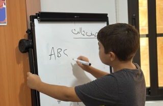 A young boy writes on a white board