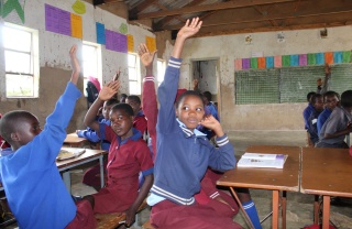 Kids in a classroom with their hands up