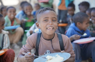 A happy boy eating a bowl of food
