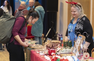 A woman looks at products at a stall at a Christmas market while another woman stands behind the stall