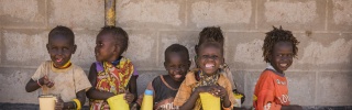 A line of children sitting against a wall eating