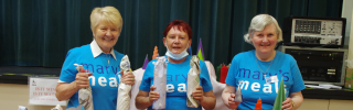 Three members of Blairgowrie volunteer group at a stall with crafts in Mary's Meals blue t-shirts