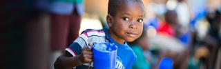 Child in Malawi holding mug of porridge