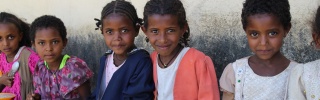 Children sitting on a wall eating bowls of food