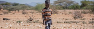 A small boy walks over stones on dry land in Kenya