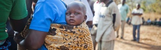 A small baby sitting in a sling on the back of a woman