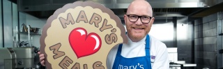 Chef Gary Maclean with Mary's Meals blue apron on and biscuit prop