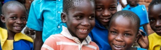 Young children holding blue Mary's Meals porridge mugs and smiling for camera