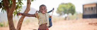Boy jumps in celebration by a tree in Zambia