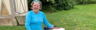 Woman in blue t-shirt standing in campsite with trailer and sign