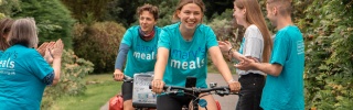 Jacob and Lucia cycling and being cheered on by supporters