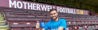 Football Stephen O'Donnell sitting in stand of football stadium in blue Mary's Meals t-shirt with blue Mary's Meals mug