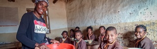 A volunteer cook serves food to children in a classroom