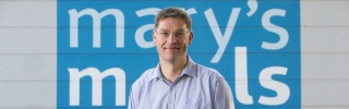Founder of Mary's Meals, Magnus MacFarlane-Barrow (man) standing in front of Mary's Meals logo