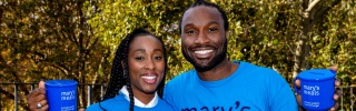 Scarlette and Stuart Douglas standing together smiling holding Mary's Meals mugs and wearing Mary's Meals t-shirts