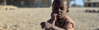 A child in Ethiopia sits on the dusty ground.