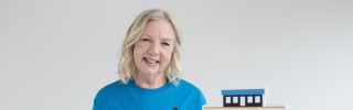 Deborah Meaden wearing a Mary's Meals t-shirt holding a sign which reads 'Sponsor A School with Mary's Meals'