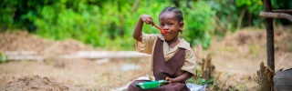 A girl sitting outside eating Mary's Meals in Liberia