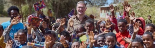 Magnus MacFarlane-Barrow standing alongside a group of happy school children in Ethiopia