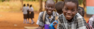 Children smiling while leaning on wall with mugs of Mary's Meals porridge in Zambia