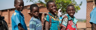 Four boys outside in Malawi standing with mugs