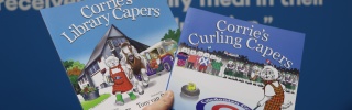 A hand holds up copies of two picture books, Corrie's Library Capers and Corrie's Paper Capers