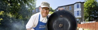 Gary Maclean holds a piece of meat over a BBQ with food cooking