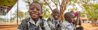 Boys in Zambia sit outside with mugs of Mary's Meals