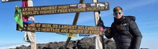 Teenager Lochlan stands at a sign signalling that he is at the summit of Mount Kililmanjaro