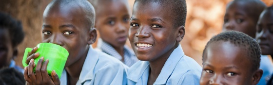 Three Zambian boys in school uniform holding a mug of porridge