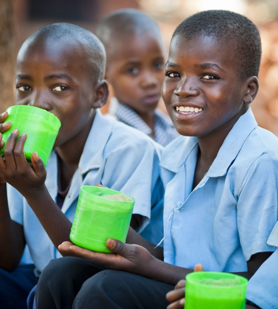 Three Zambian boys in school uniform holding a mug of porridge