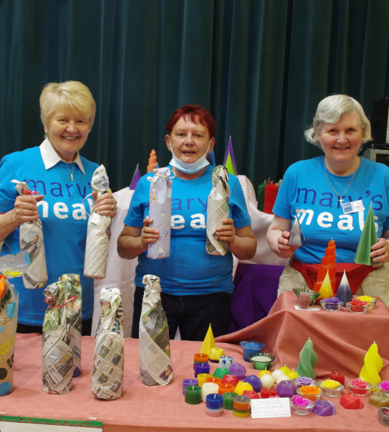 Three members of Blairgowrie volunteer group at a stall with crafts in Mary's Meals blue t-shirts