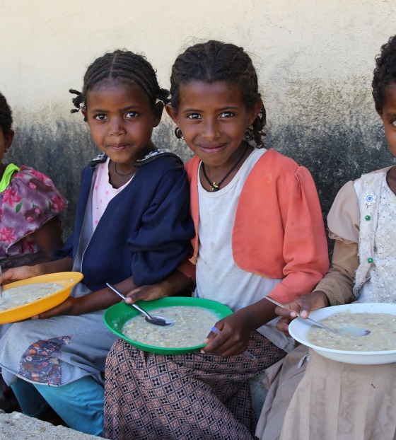 Children sitting on a wall eating bowls of food