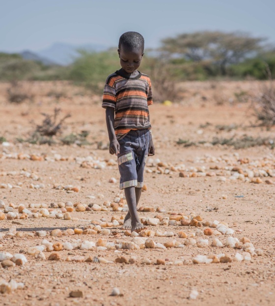 A small boy walks over stones on dry land in Kenya