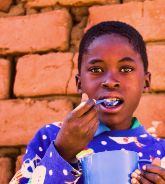 A boy in a Christmas jumper enjoys food from Mary's Meals
