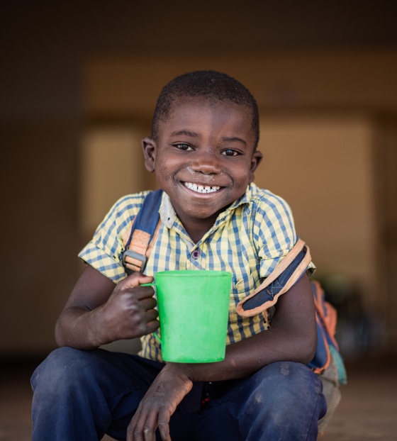 Smiling child holding mug of Mary's Meals porridge