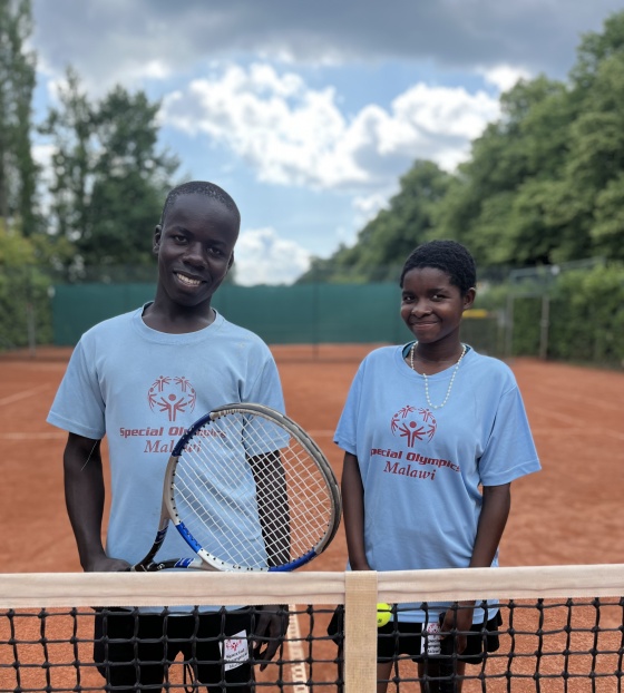 Patrick and Hannah standing behind a tennis net holding rackets