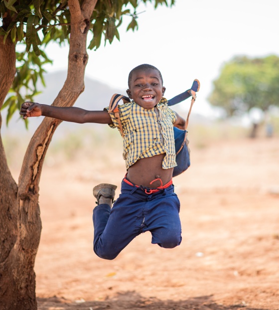 Boy jumps in celebration by a tree in Zambia