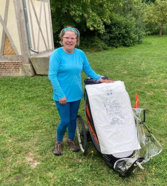 Woman in blue t-shirt standing in campsite with trailer and sign