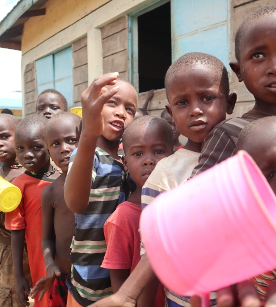 children in Kenya queuing for their lunch, mugs in hand