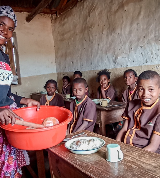 A volunteer cook serves food to children in a classroom
