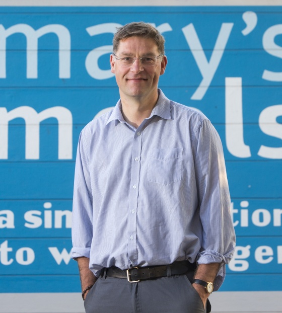 Founder of Mary's Meals, Magnus MacFarlane-Barrow (man) standing in front of Mary's Meals logo