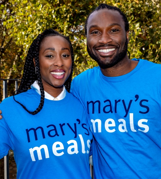 Scarlette and Stuart Douglas standing together smiling holding Mary's Meals mugs and wearing Mary's Meals t-shirts